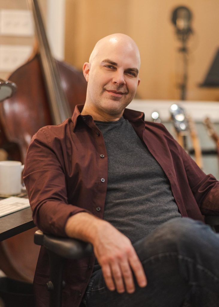 Music producer Will Robertson sitting in a chair at his desk and smiling
